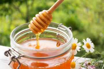 Pot Of Honey And Wooden Stick Are On A Table outdoors