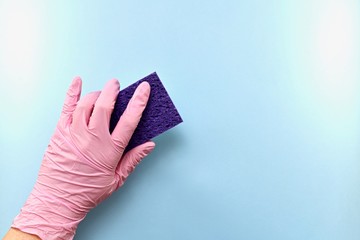 Purple household sponge made of natural washcloths, in the left hand in a pink rubber glove. On the blue background on the left in the center presses the washes under the slope.