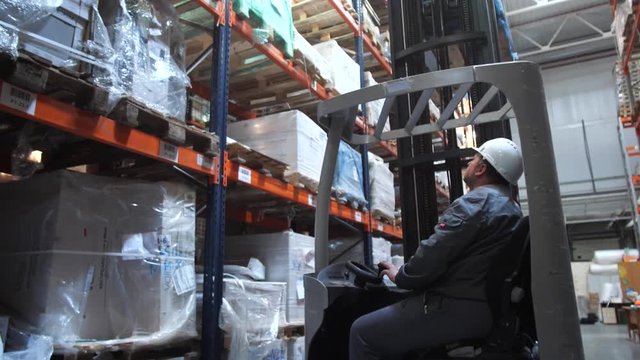 Logistics warehouse. A man moves in a special car, raises the goods on the shelf. 4K Slow Mo