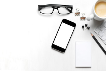 on a white table background from above smartphone, eye glasses, coffee cup pen and paper isolated 