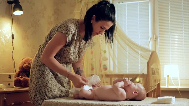 Mom changes the diaper baby. Beautiful white girl mother changes the diaper to her little child, the action takes place in the nursery