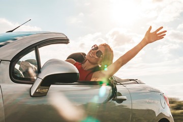 happy young woman enjoying a ride in a convertible car. hand greeting. The concept of road travel...
