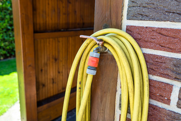 A garden yellow hose connected to a tap protruding from a farm building against a background of...