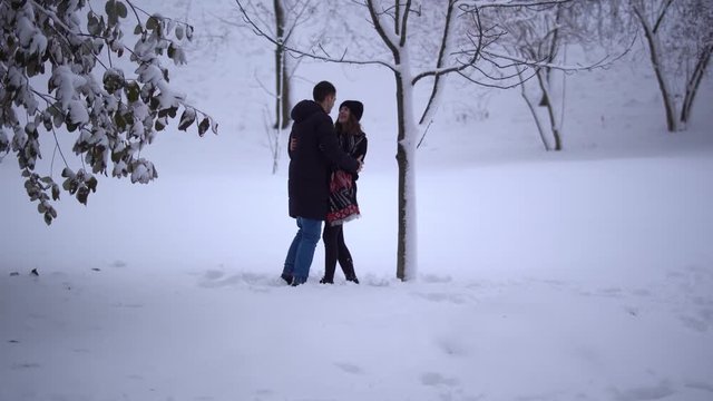 Cute young man and girl spend their leisure time in a snow-covered park. Date of young couple. Happy couple in love enjoy time together.