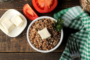 Buckwheat. Porridge with a piece of butter in a glass plate on a brown wooden table. breakfast, healthy food. top view