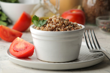 Buckwheat. Porridge cereals with parsley in a white ceramic bowl and tomato on a bright table. breakfast, healthy food.