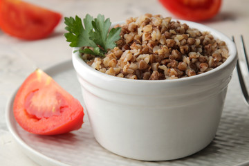 Buckwheat. Porridge cereals with parsley in a white ceramic bowl and tomato on a bright table. breakfast, healthy food.