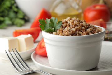 Buckwheat. Porridge cereals with parsley in a white ceramic bowl and tomato on a bright table. breakfast, healthy food.