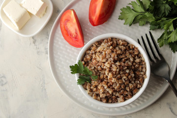 Buckwheat. Porridge cereals with parsley in a white ceramic bowl and tomato on a bright table. breakfast, healthy food. top view