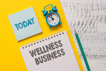 Text sign showing Wellness Business. Business photo showcasing Professional venture focusing the health of mind and body Spiral notepad paper sheet marker alarm clock retro wooden background