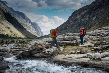 man and woman backpacker in the Andes of Peru cross a wild mountain stream