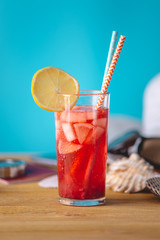 Glass of red lemonade drink with lemon and straw on the table. Concept of a bright summer Sunny holiday in the resort.