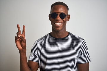 Naklejka premium African american man wearing striped t-shirt and sunglasses over isolated white background smiling with happy face winking at the camera doing victory sign. Number two.
