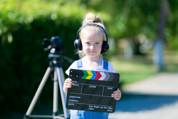A little girl in headphones with a TV numerator in her hands is standing next to the camera on a...