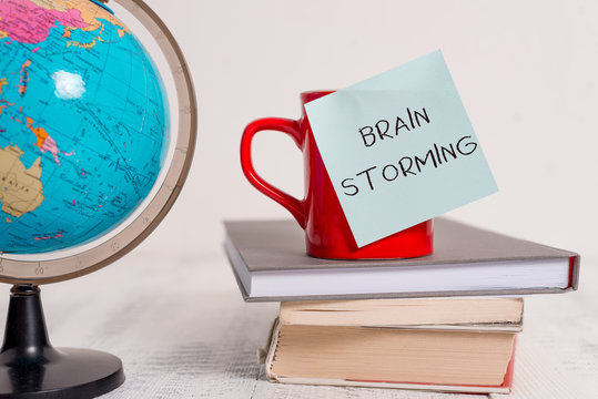 Writing note showing Brain Storming. Business concept for Stimulating creative thinking Developing new ideas Discussion Globe map world earth cup blank sticky note stacked books wooden table