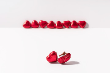 Heart shape chocolates wrapped in red foil on white background. Valentines day gift. Love and parting concept. Copy space.