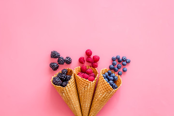 Fresh berries in waffle cones on pink background top view mock up