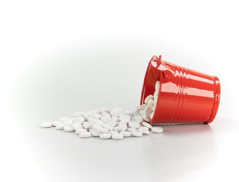 White pills, tablets in red metal bucket on white background.