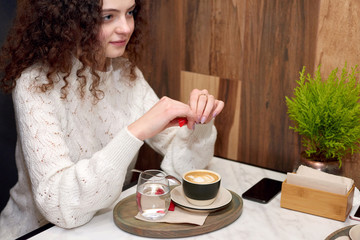 Curly hair caucasian girl with blue eyes adding sugar to coffee