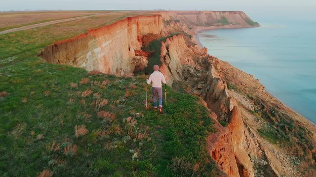 Aerial view of a young man hiking on the cliff at the seaside enjoying the view