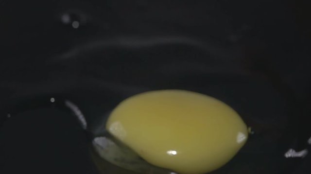 The contents of the broken egg, yolk and protein, slowly slide on the black surface. The concept crack an egg for Breakfast and fresh eggs. Super slow motion 1000 fps