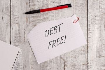 Word writing text Debt Free. Business photo showcasing does not owning any money to any individual or companies Torn paper and notebook sheet with a pen placed on top of wooden table