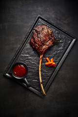 large beef tomahawk steak with sauce at black stone background garnished with french fries.