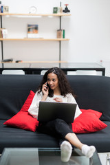 Portrait of a woman speaking on cellphone in front of her laptop computer at home