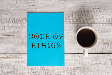 Conceptual hand writing showing Code Of Ethics. Concept meaning basic guide for professional conduct and imposes duties Stationary placed next to a coffee cup above wooden table