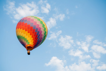 Colorful hot air balloon moving up in blue sky.