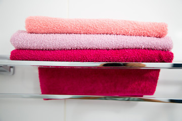 A stack of multi-colored towels on a metal shelf. Horizontally.