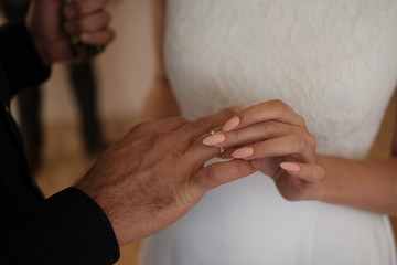  female hand in bridal dress puts a ring on a man's hand