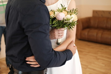  male hand embraces a female figure in a wedding dress with a bouquet of flowers