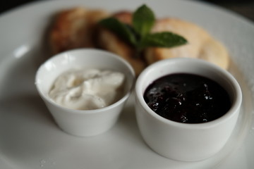  curd cheese cakes and pialas with jam and sour cream on a plate on a table in daylight