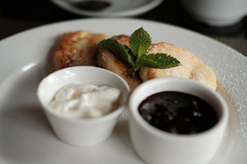  curd cheese cakes and pialas with jam and sour cream on a plate on a table in daylight