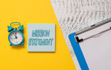 Conceptual hand writing showing Mission Statement. Concept meaning Formal summary of the aims and values of a company Notepad colored paper sheet alarm clock wooden background