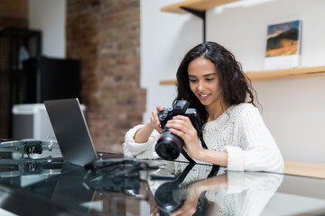 Beautiful woman photographer posing with her camera. The girl work at home with a laptop and a...