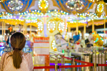 Obraz premium Young woman looking at the amusement park carousel