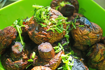 Mushrooms champignons fried on a brazier on a picnic lie on a green plate seasoned with greens