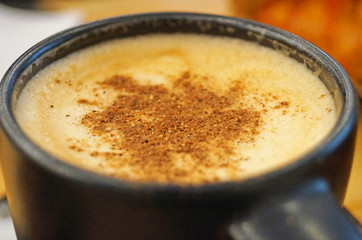 Cappuccino with a thick crema sprinkled with cinnamon poured into a black cup on the table