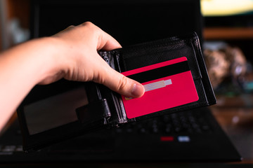 Hand holding a wallet and credit card with a laptop in the background