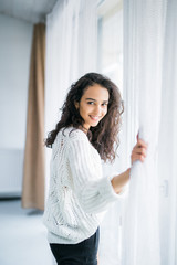 People and hope concept. Happy woman opening window curtains