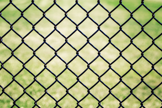 Closeup of black metal netting wire mesh fence against green field meadow. Texture pattern surface background of  chain link wire-mesh rabitz.