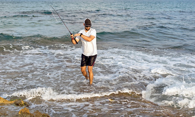 Fisherman standing at the seashore hooks a fish.