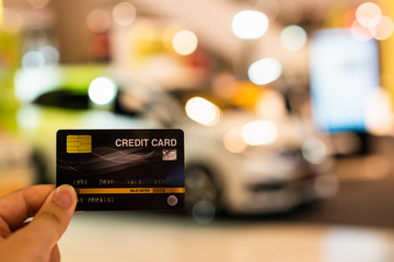 Hand holding credit card with blur car showroom in shopping mall , shopping and retail,  Payment by credit card for buy new car concept.
