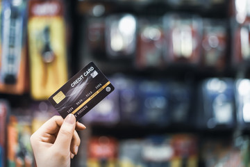 Hand holding credit card with blur supermarket, shopping and retail concep