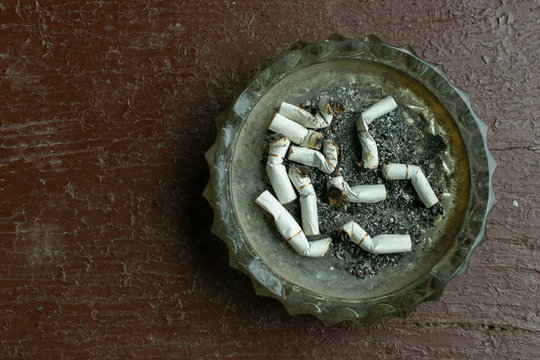 crystal ashtray with cigarette butts and ash on a brown wooden table, view from the top