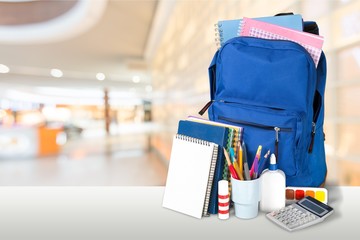 Colorful school supplies in backpack on blurred background