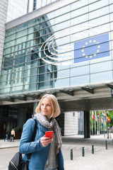 A young woman stands with a telephone in her hands opposite the European Parliament building in...