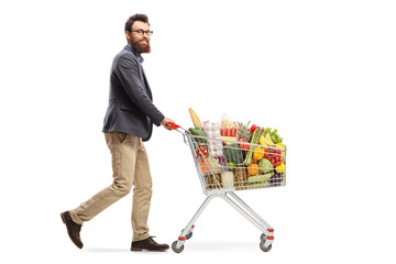 Bearded man pushing a shopping cart with food products and looking at the camera